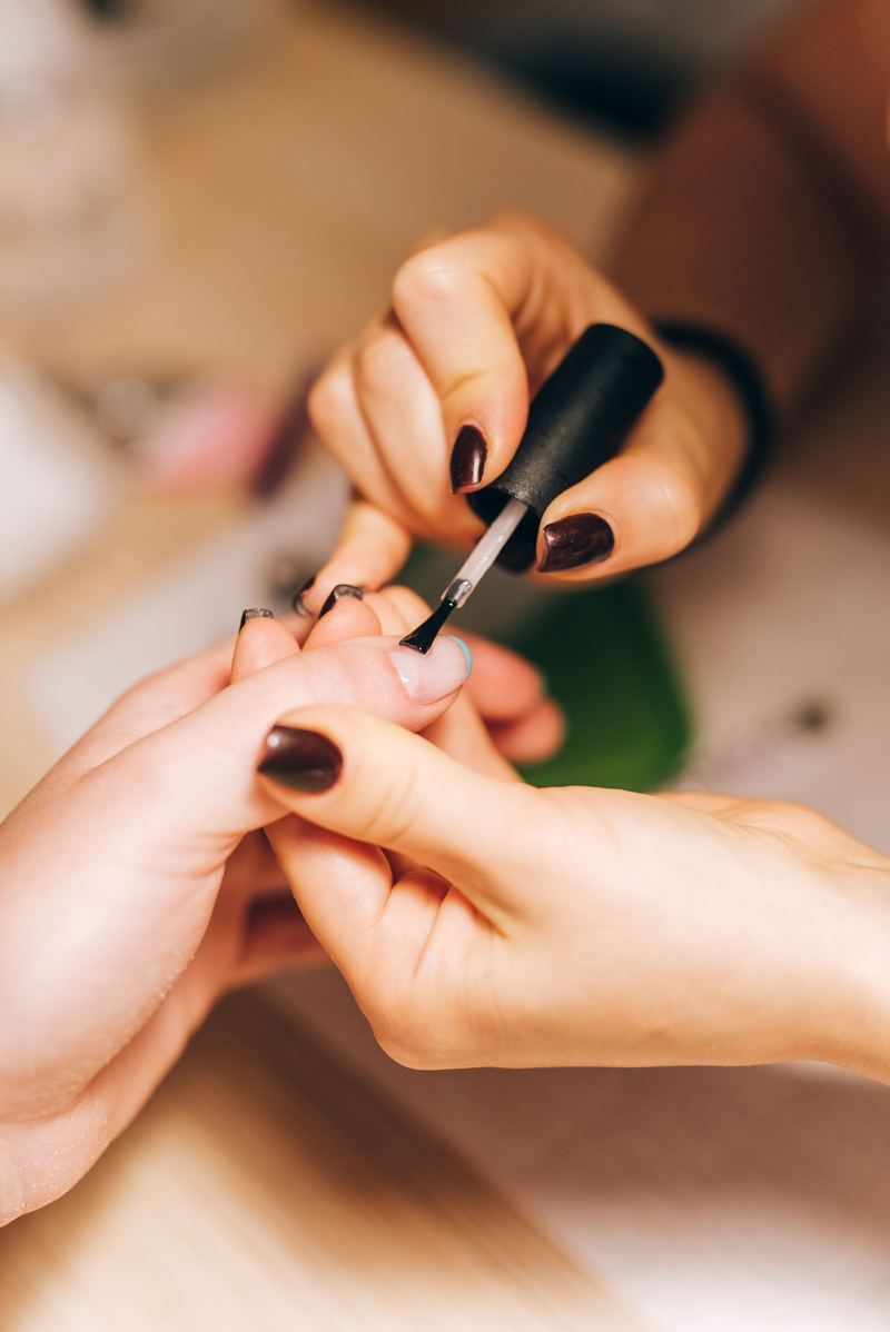 Manos con esmalte oscuro mientras les pintan las uñas en un salón