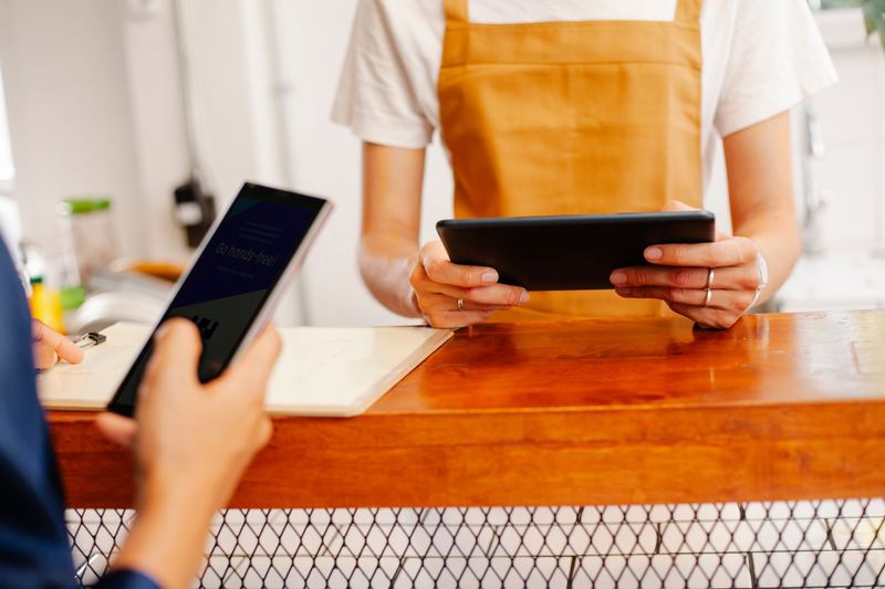 Una persona con delantal sostiene una tablet sobre el mostrador de una cafetería